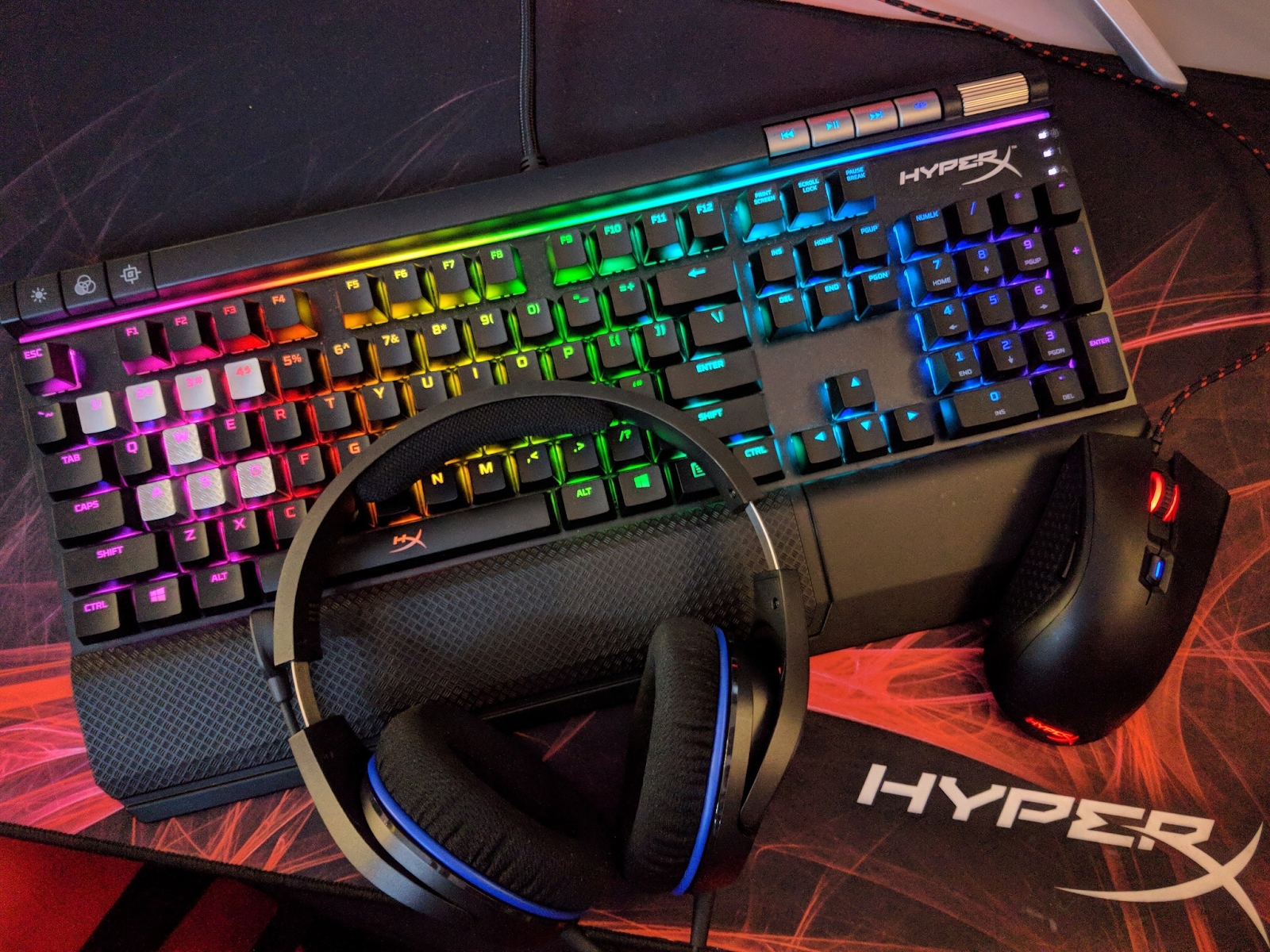 A HyperX headset, RGB keyboard and mouse sit atop a HyperX desk mat