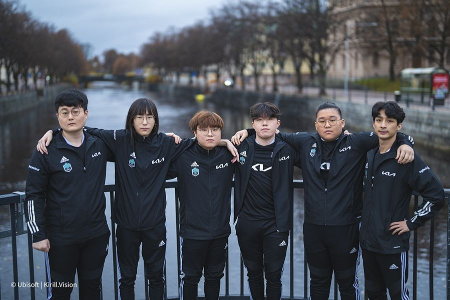 The roster for Damwon Gaming (DWG KIA) stand in their team jerseys with arms over each others shoulders.